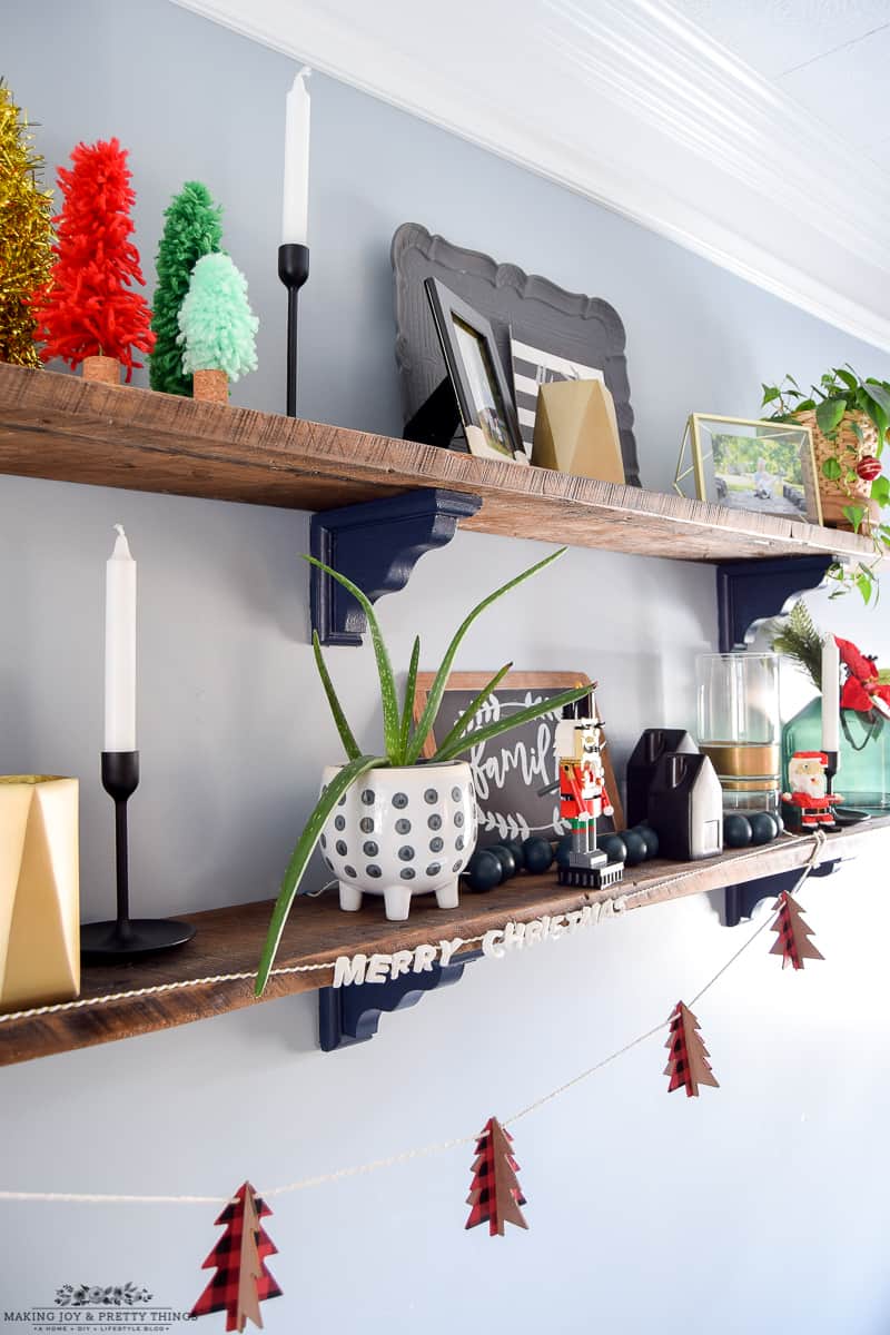 Greenery and trays and other decor all on rustic farmhouse shelves to add Christmas spirit to a dining room.