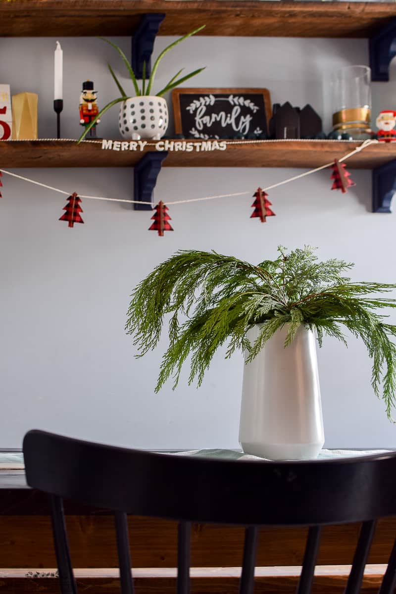 Decorating shelves with a Merry Christmas garland contrasted with a vase full of cedar trimmings as a center piece