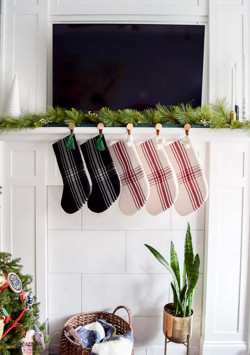 5 modern plaid stockings hung on a white mantel with a modern brass stocking holder.