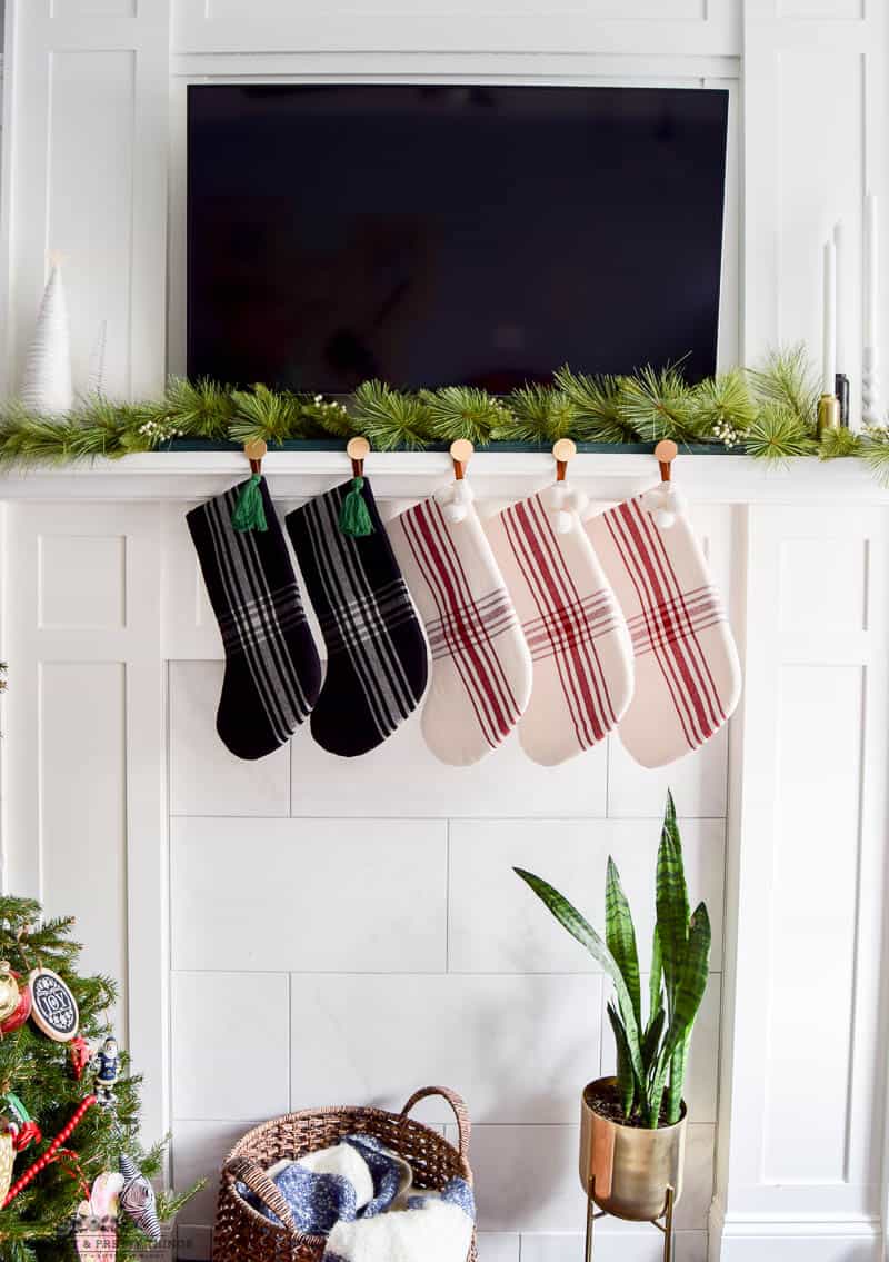Decorating a mantel in a living room with garland and other Christmas decor to show off new stocking holder