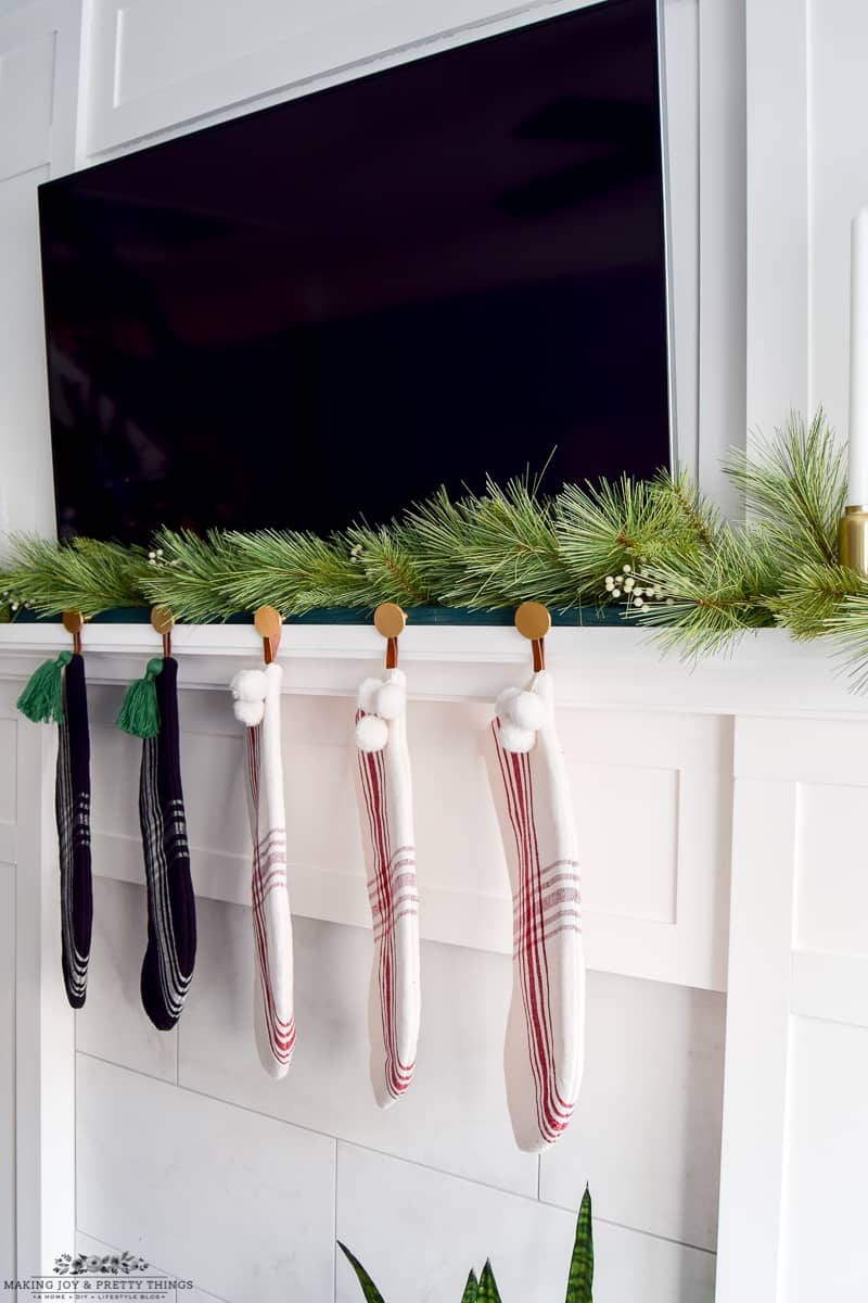 Living room mantel decorated with a DIY stocking holder, garland, and candlesticks for a modern Christmas look