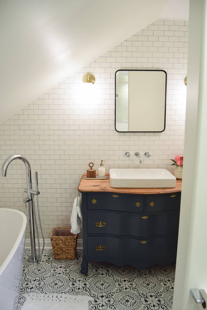 The gorgeous modern vintage bathroom vanity, with an updated vintage dresser, inlay porcelain sink, wall-mounted faucet, sconces, and a black-framed mirror.