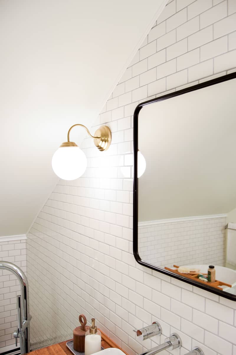 Mixing metals in our vintage modern bathroom: brass globe wall sconces next to a sleek matte black framed mirror hanging on white subway tiled walls.