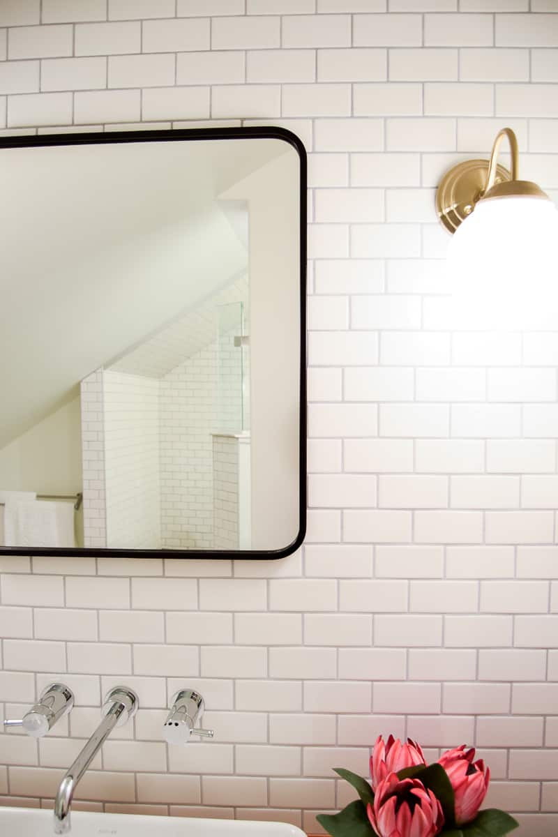 The modern theme of our master bathroom continues with a sleek matte black framed mirror hung on our white subway tiled bathroom walls.