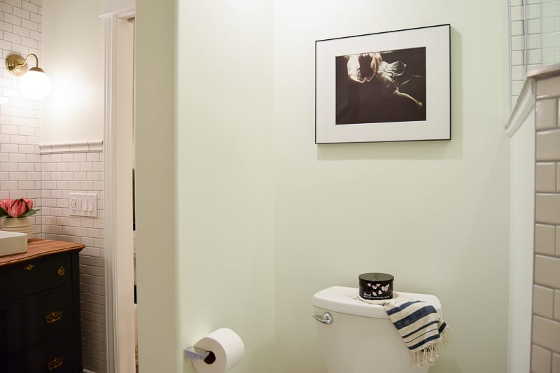 The toilet nook in our modern vintage bathroom is simple: white walls, and a framed photograph hanging on the wall.