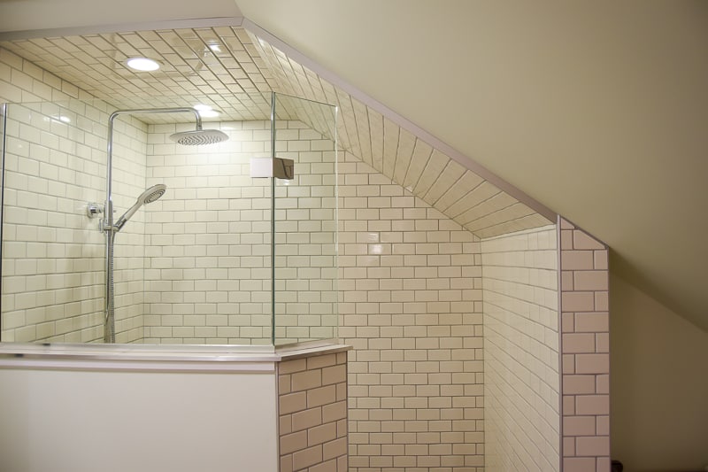 The walk-in shower corner of our vintage modern bathroom was completely tiled in white subway tile and shower glass, with a rainfall shower head, and slanted walls.