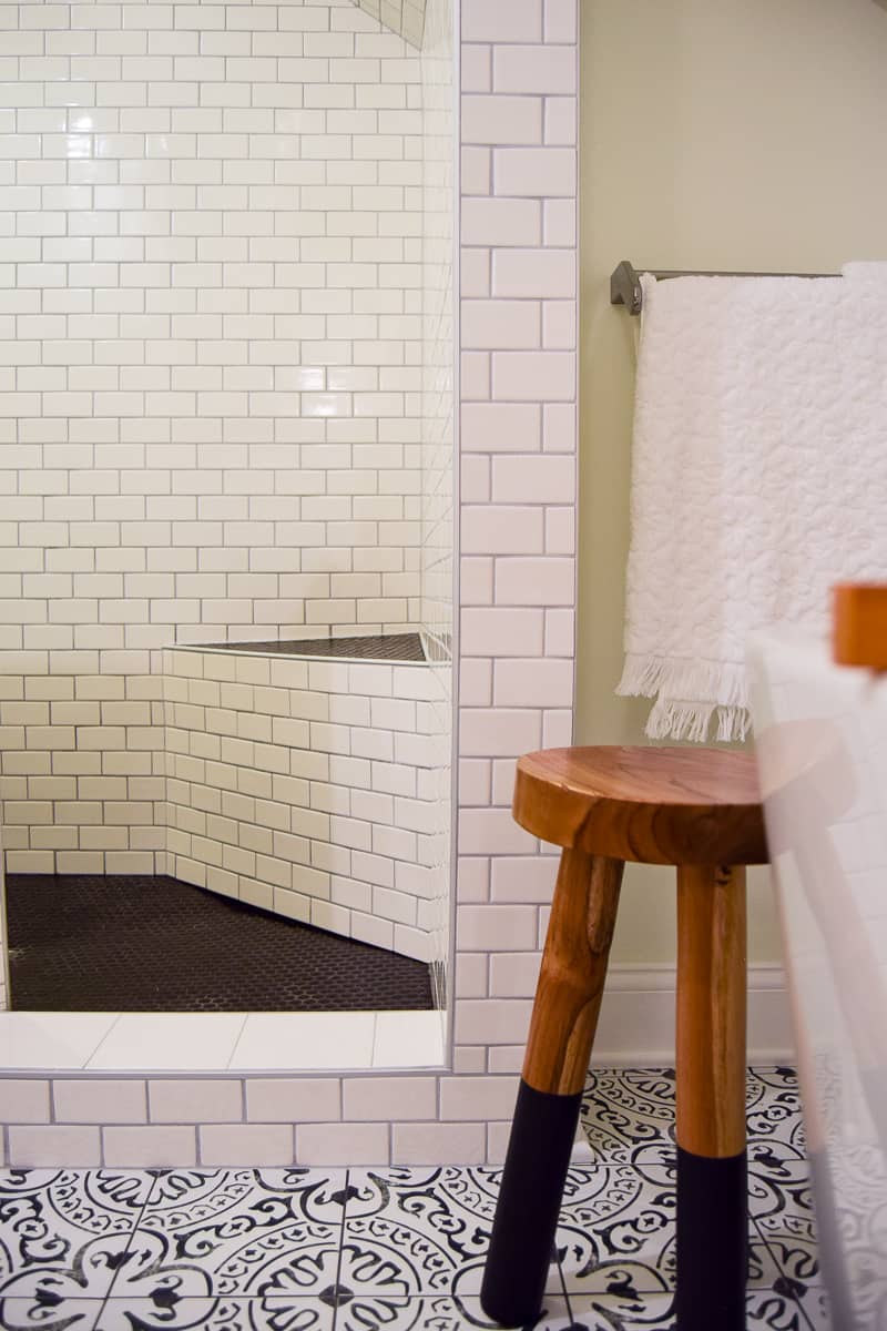 A look at the gorgeous subway tiled walls in our walk-in shower, with a slanted ceiling, black penny floor tiles, and wall-mounted towel rack.