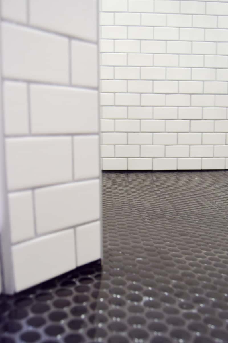 A close up look at the gorgeous black penny floor tiles and white subway tiled walls in the walk-in shower in our upgraded vintage modern master bathroom.