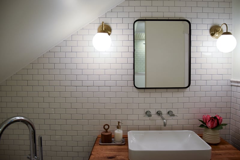 A complete look at the top of our upgraded bathroom vanity, with an inlayed porcelain sink, wall-mounted faucet, modern black framed mirror, and globe wall sconces.