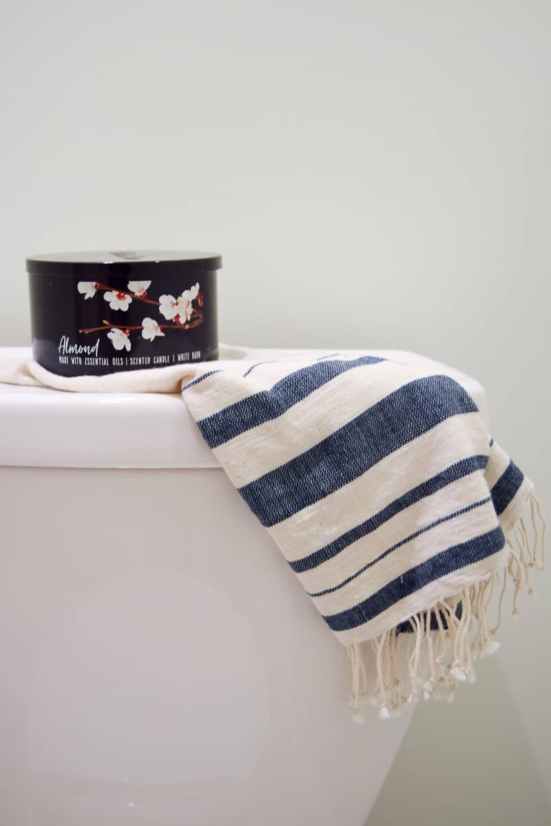 Some of the simple decor in our vintage modern bathroom - an almond scented candle and blue and white linen hand towel sits on the back of the toilet.