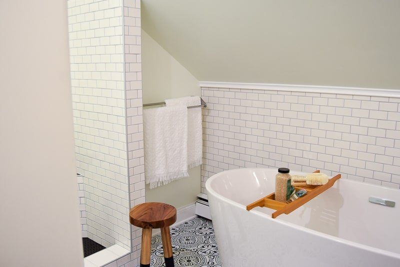 The bathtub and walk-in shower corner of our vintage modern bathroom, with slanted ceiling, subway tiled walls, deep-soak bathroom, and black and white tiled walls.