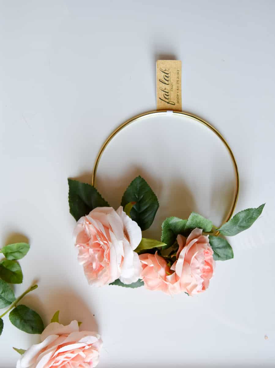 Three peony flower heads sit arranged on a gold macramé hoop. Arranging the flowers how you want them to look is the first step to making a flower crown.
