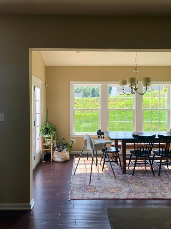 A bright and sunny dining room area with large windows, french doors, and a large natural wood dining table with chairs and a high chair.