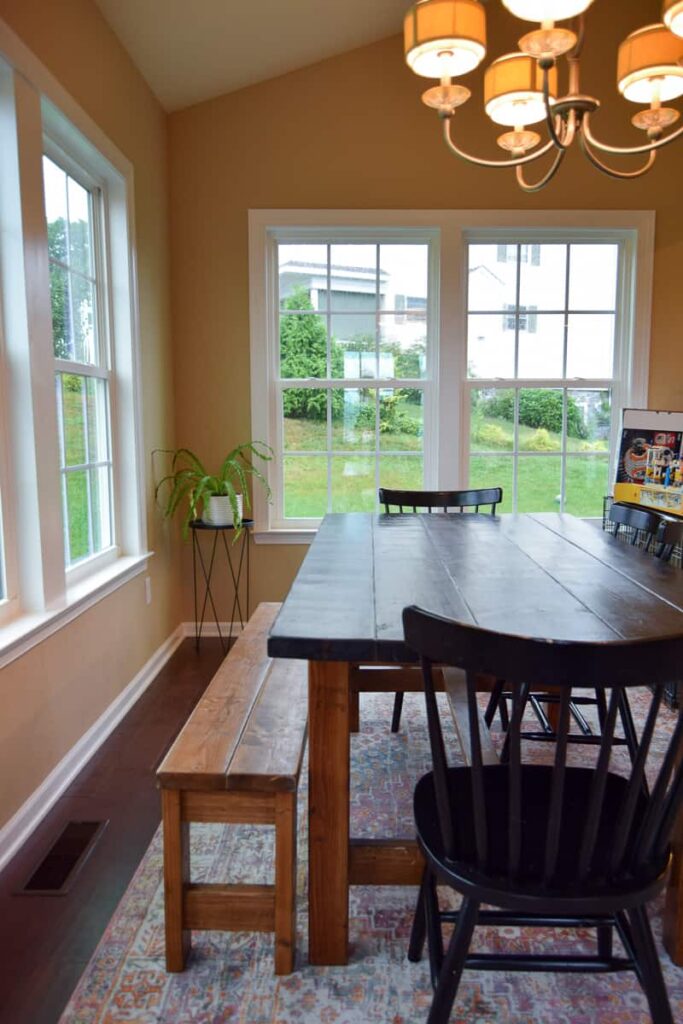 Another angle of our dining room looks out into the backyard through large double hung windows. A large dark wood dining table with bench seats and chairs sits in the middle of the room.