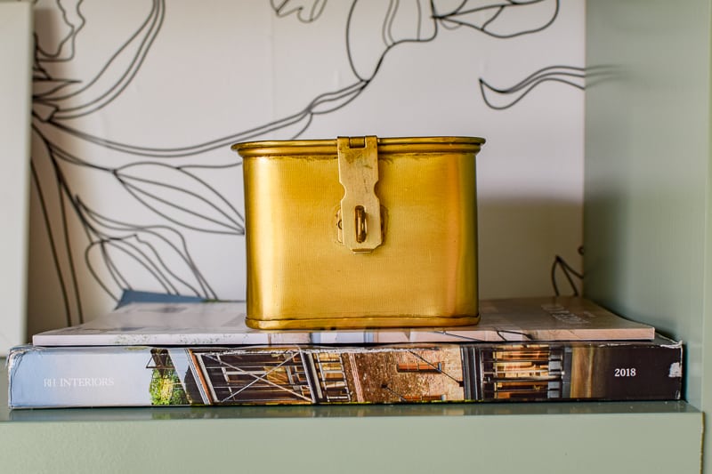 Gold tin on top of books to create contrast on open shelves with a wallpaper background