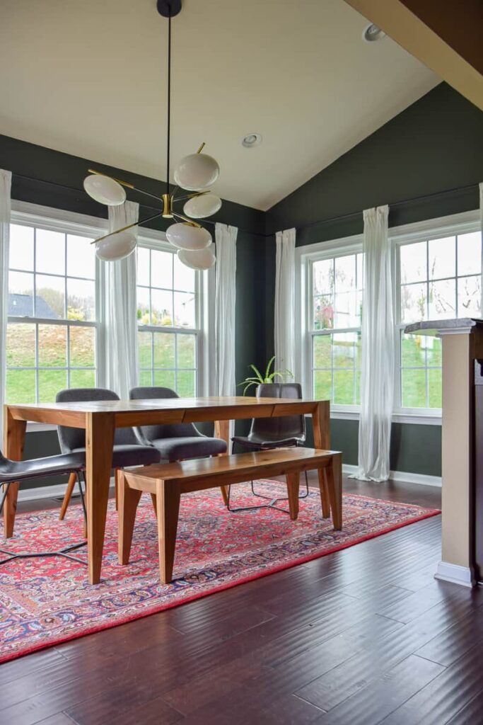 A photo of a kitchen with table and chairs, chandelier, window with curtain and painted wall.