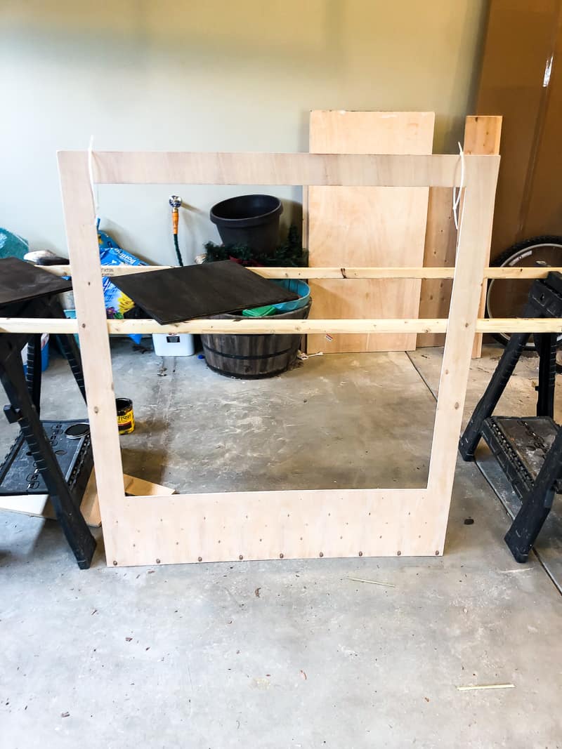 A large wooden polaroid frame leans against strips of wood on plastic work horses.