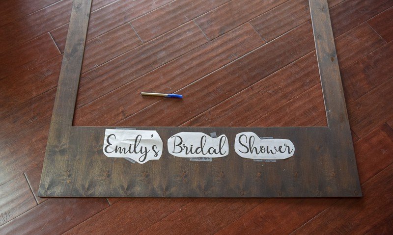 Three pieces of paper, each with one word spelling out "Emily's Bridal Shower" are taped to the bottom of a dark wood polaroid frame.