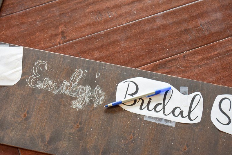 Tracing lettering onto a wooden polaroid frame. The word "Emily's" is traced in chalk onto a dark wood frame. A piece of paper that reads "Bridal" is taped to the frame.