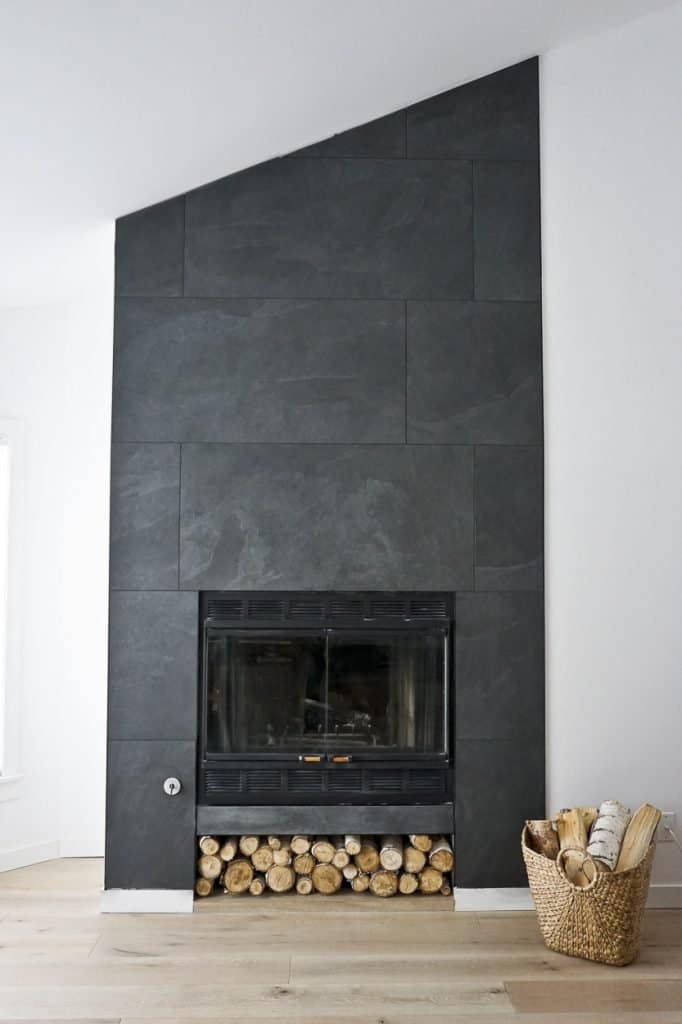 Wood storage and a slant fireplace that was updated with black tile completely from floor to ceiling