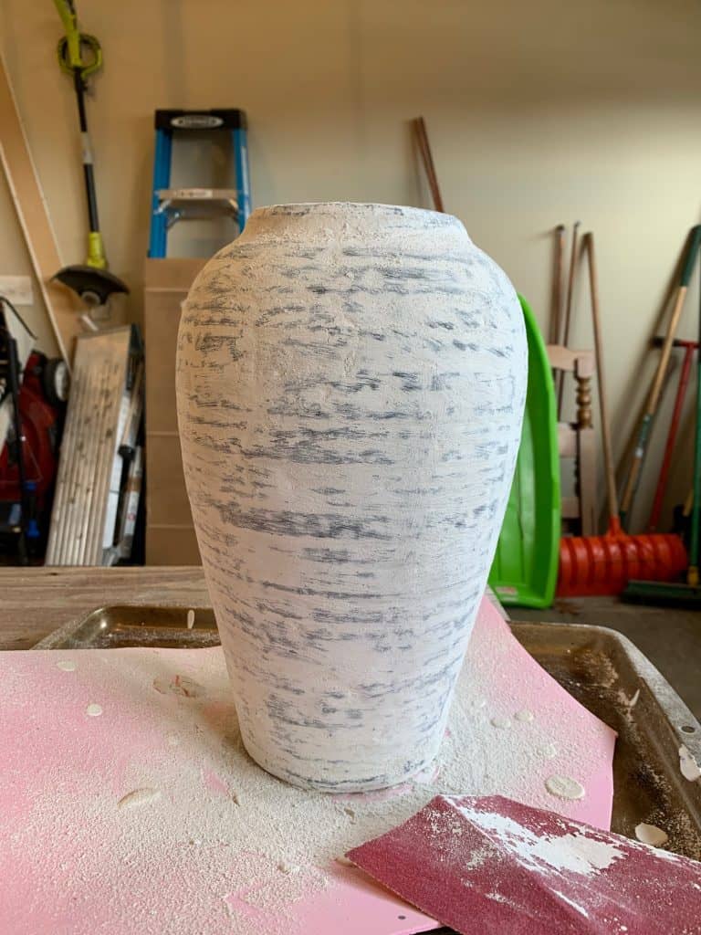 A large vintage vase covered in sanded down plaster, surrounded  with plaster dust and sandpaper.