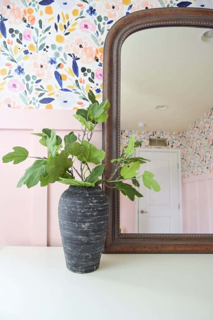 A closer look at the aged black pottery, filled with faux leaves, on a dresser with a large mirror.