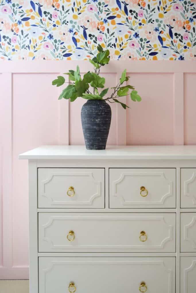 This gorgeous aged black vase stands out against a pink wall and white dresser in a little girl's room.