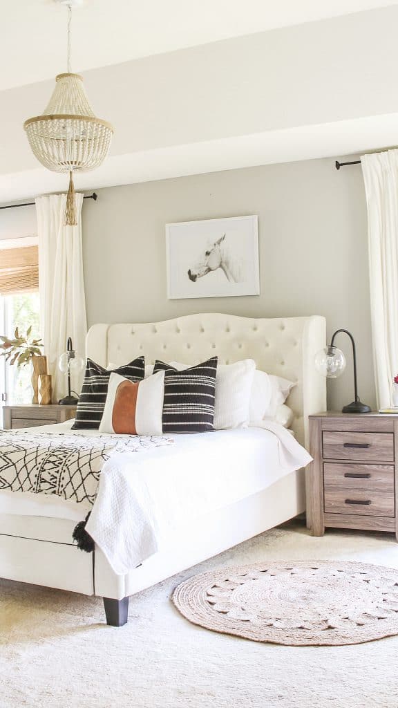 A master bedroom with a white upholstered queen sized bed up against a gray wall. The wall is painted with Repose Gray SW 7015 from Sherwin-Williams, the perfect grey-beige color.