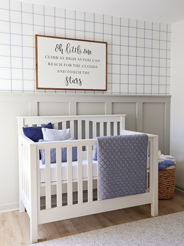 A baby's crib against an accent wall painted in the serene hue of Mindful Gray with blue check wallpaper above it