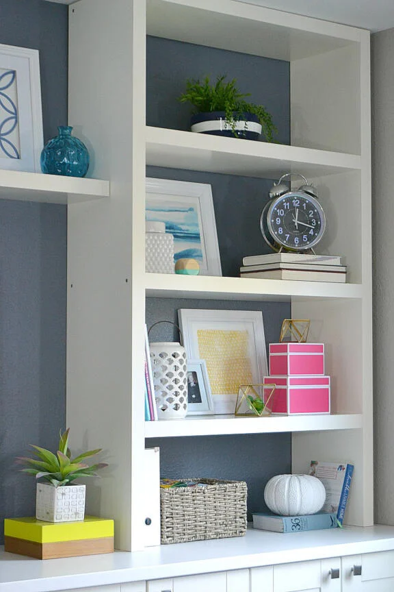 A photo featuring built-in shelves with a backdrop painted in the eye-catching Sherwin Williams Distance paint color enhances the display's visual appeal.