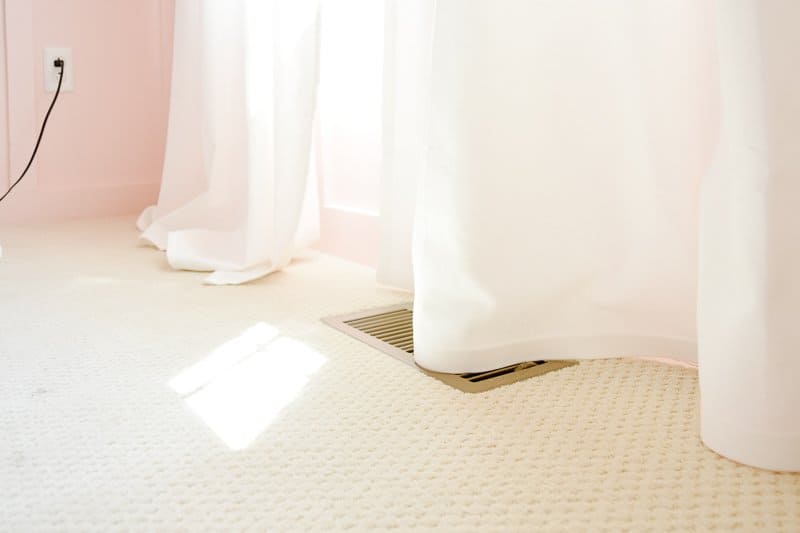 Two panels of floor length white curtains; one panel is too long and pools on the ground. The second panel has been hemmed and just barely touches the carpeted floor.