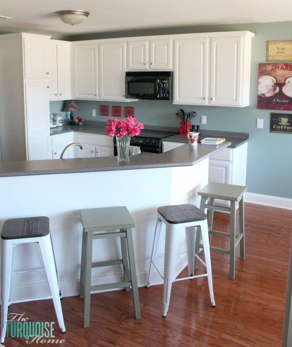 A Simply White by Benjamin Moore Paint Color kitchen area that includes a table with 4 chairs, kitchen island, and cabinets.