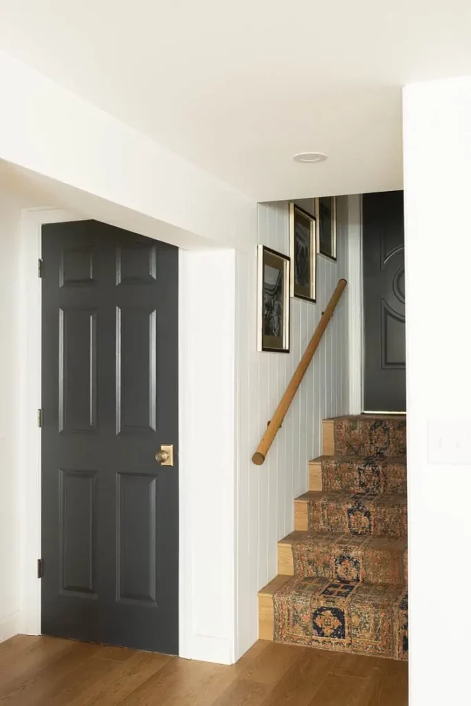 Wall painted in Simply White by Benjamin Moore with a black door, picture frame, and stairs on the side.
