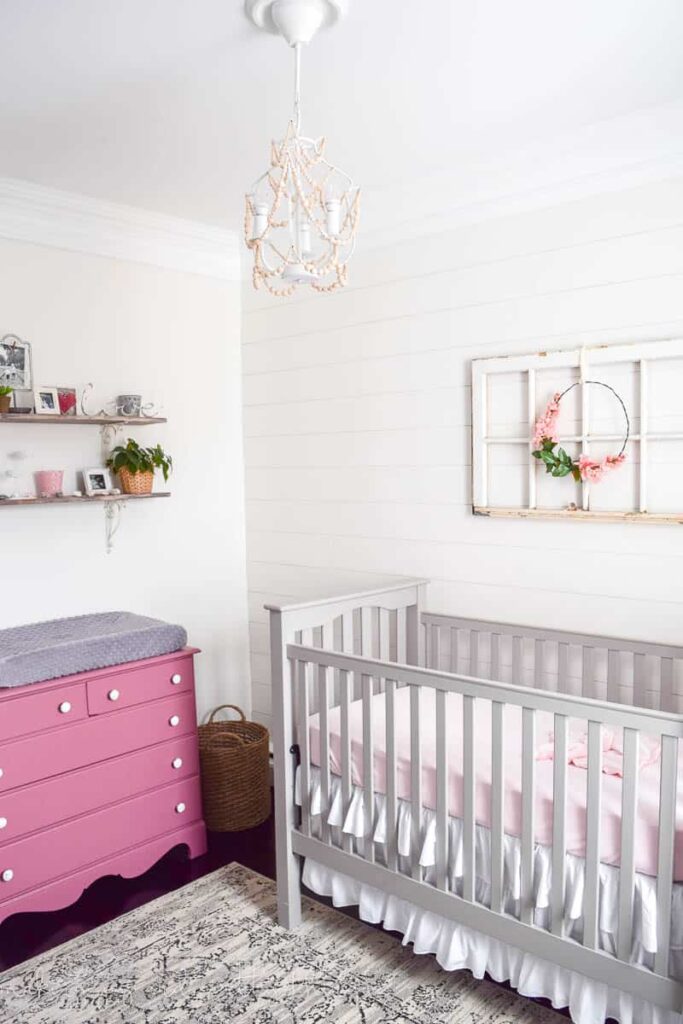Nursery with shiplap accent wall and pink dresser painted with SW Alabaster on the walls