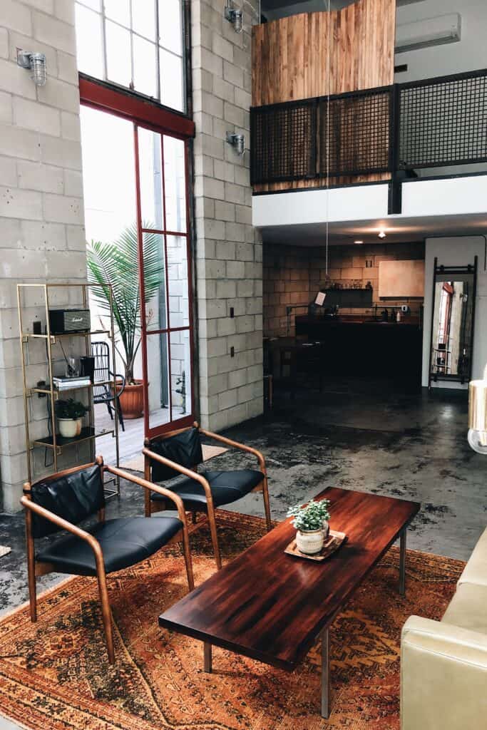 The industrial interior design has a masculine feel with loft-style vibes using high ceilings, concrete flooring, exposed brick walls, and a dark rustic color palette. This open living area demonstrates the industrial style using exposed cinder block walls, polished concrete flooring