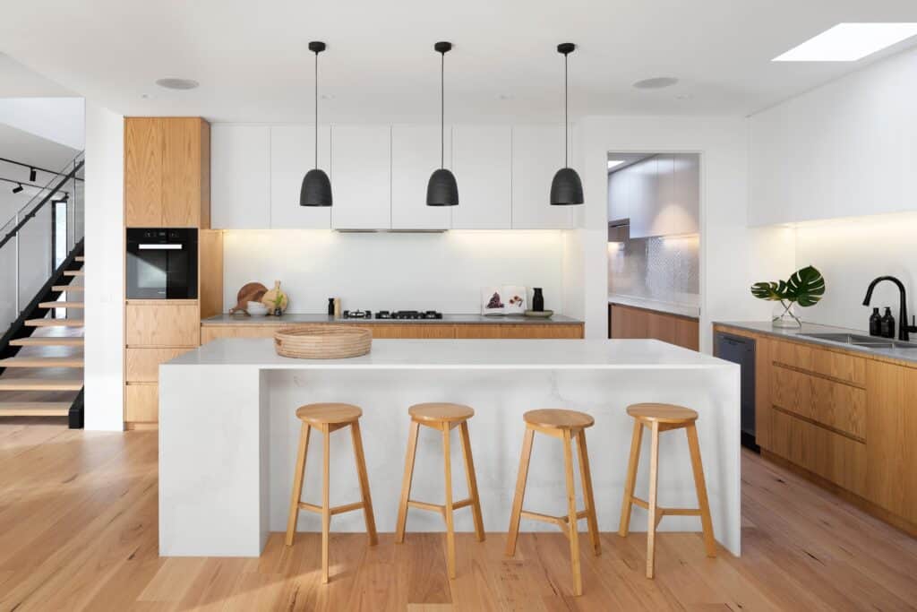 The Minimalist interior design style features simple color palettes using no more than 2-3 colors, furniture with hidden storage, minimal number of accessories and clean lines with cleared surfaces. There is no clutter to this minimalist kitchen design with white and wood cabinetry with flat faces and no hardware. The black pendant lighting contrast .