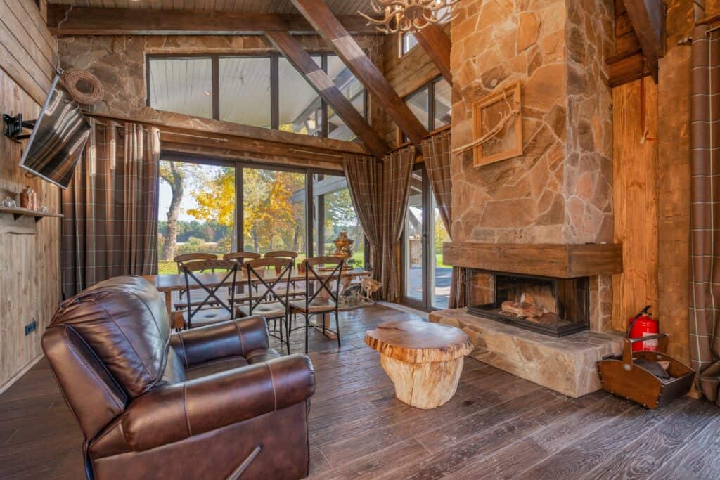 In the rustic interior design type, you will find a lot of wood textures and furniture, raw fireplaces, jute rugs and a natural color palette. This rustic living space has stone walls, wood flooring, dark leather recliner and a raw live edge coffee table.