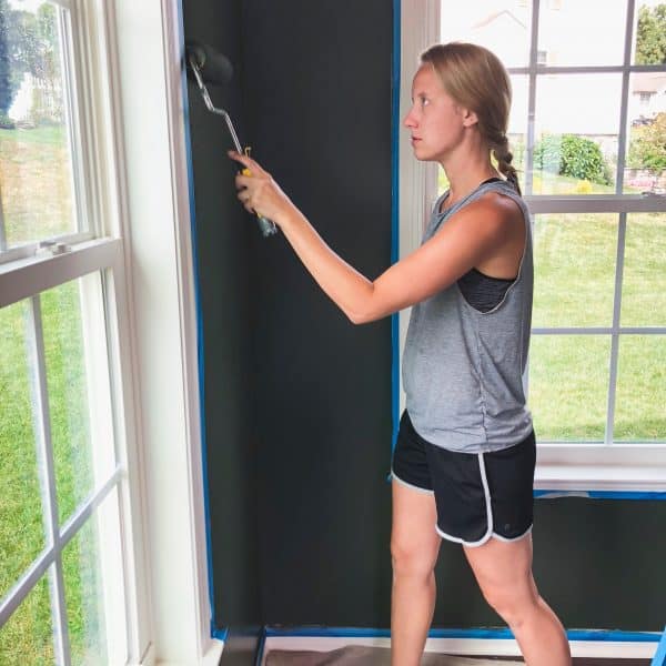 A woman applying Behr north woods paint to a wall with a roller paint brush.