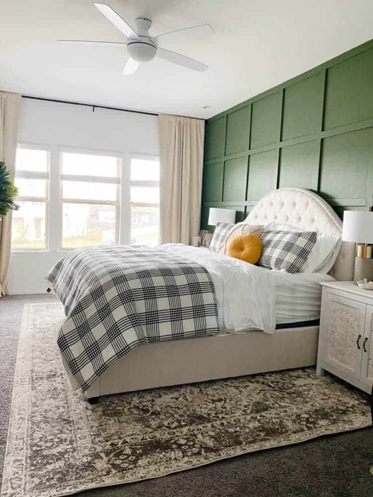 This green bedroom is styled with a  large 9x12 area rug under bed over carpet