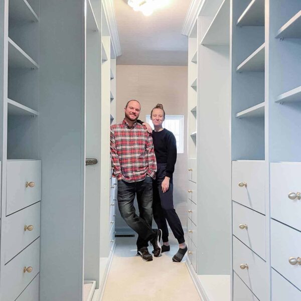 Master closet with empty IKEA built-ins painted with Benjamin Moore smoke, a blue green paint color with couple standing in middle of closet
