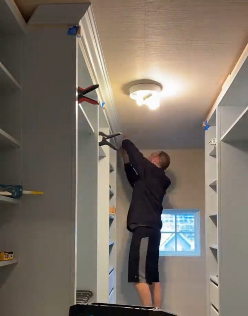 Man attaching the molding to the top edge of the IKEA Pax wardrobes in closet.