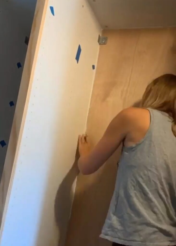 Women caulking the seams and corners of IKEA Pax wardrobes in closet before painting