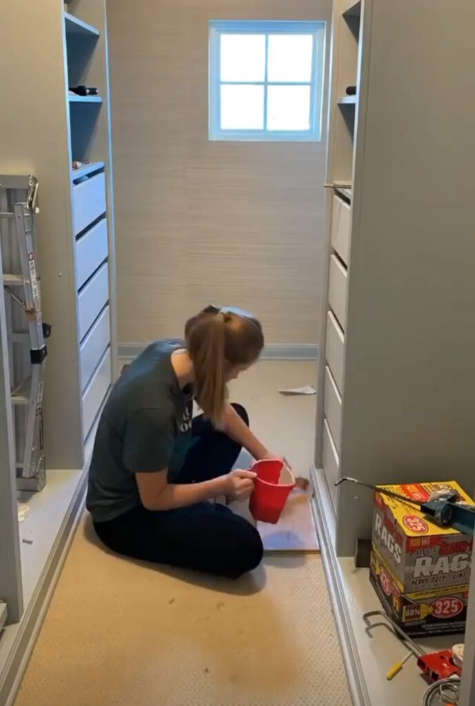 Women sitting in closet with IKEA Pax wardrobes and painting a final coat of paint along baseboards 